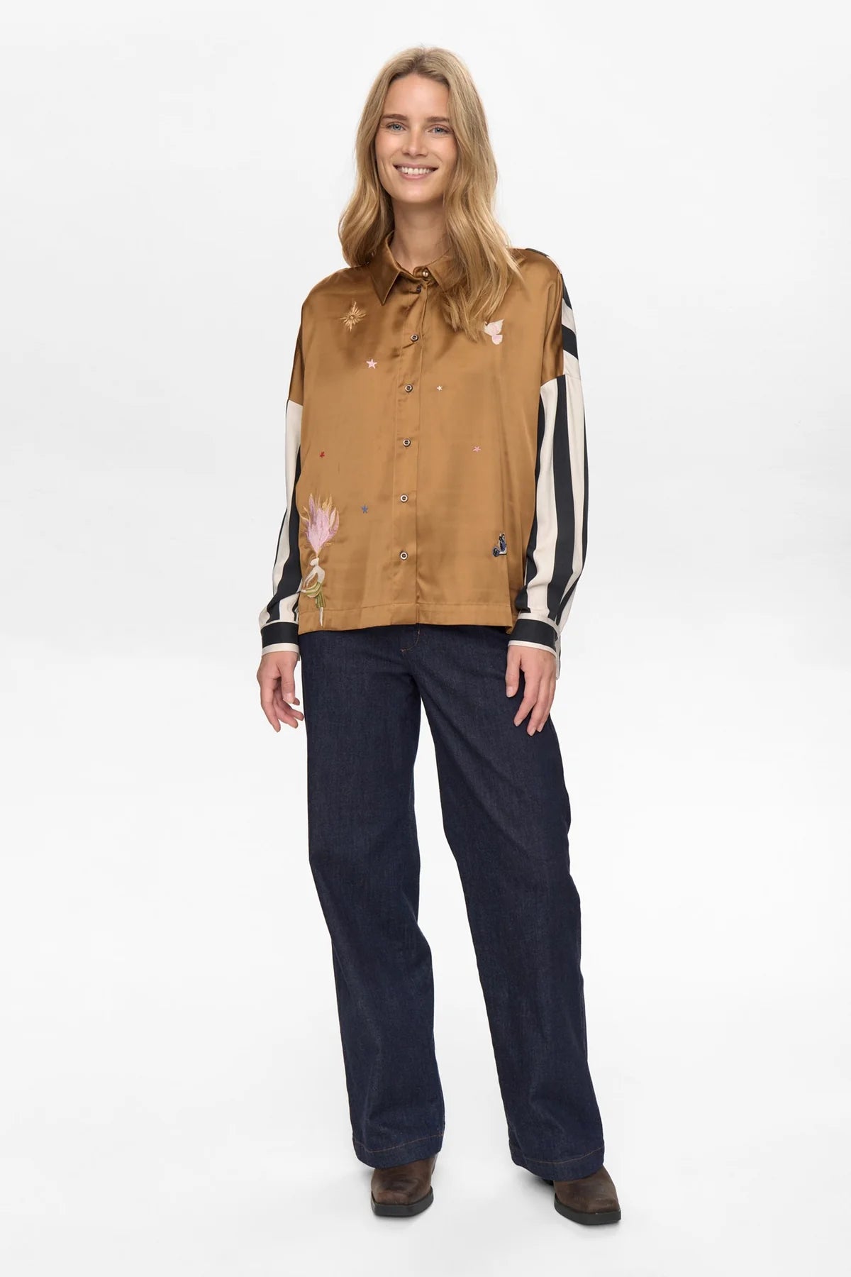 Woman wearing a tan shirt with black and white accents and dark pants on a white background