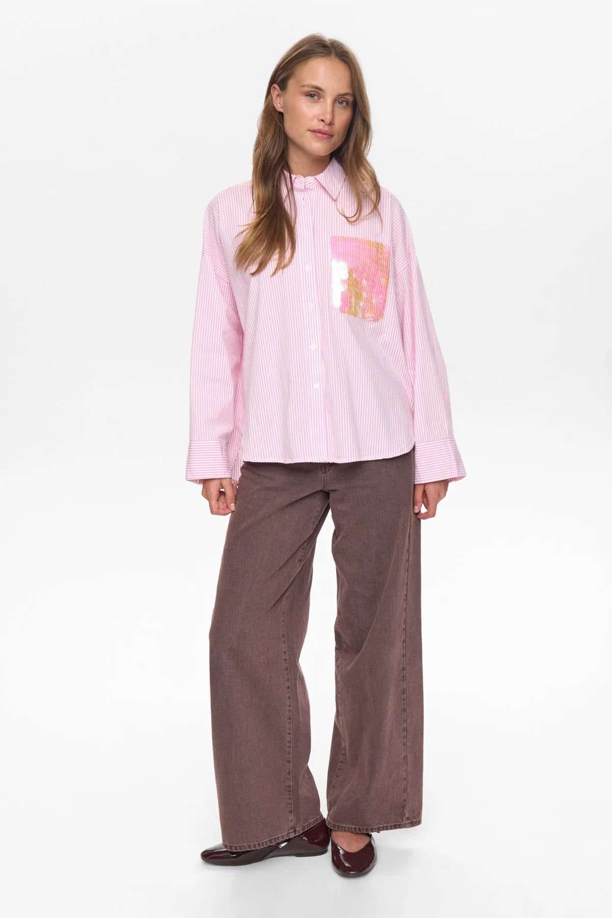 Woman wearing a pink shirt with a graphic design and brown pants on a white background