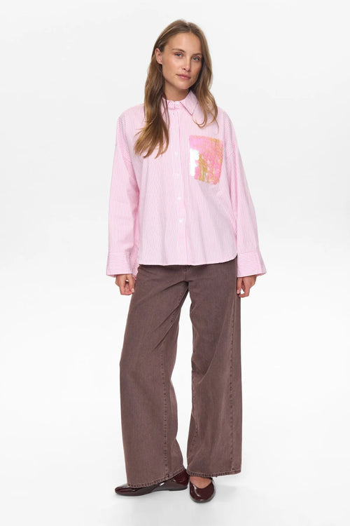 Woman wearing a pink shirt with a graphic design and brown pants on a white background