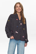 Woman wearing a black shirt with colorful embroidery and blue jeans on a white background
