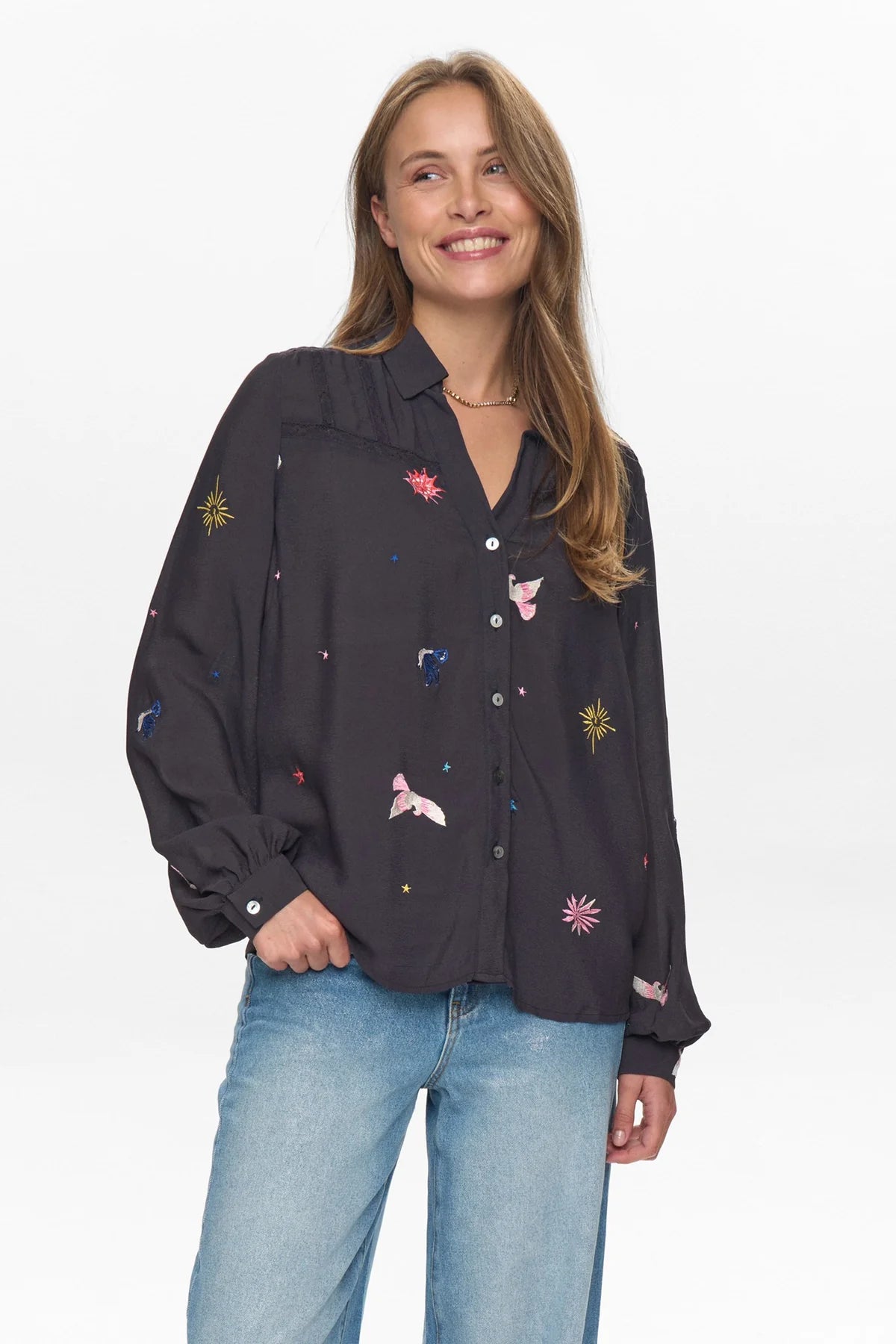 Woman wearing a black shirt with colorful embroidery and blue jeans on a white background