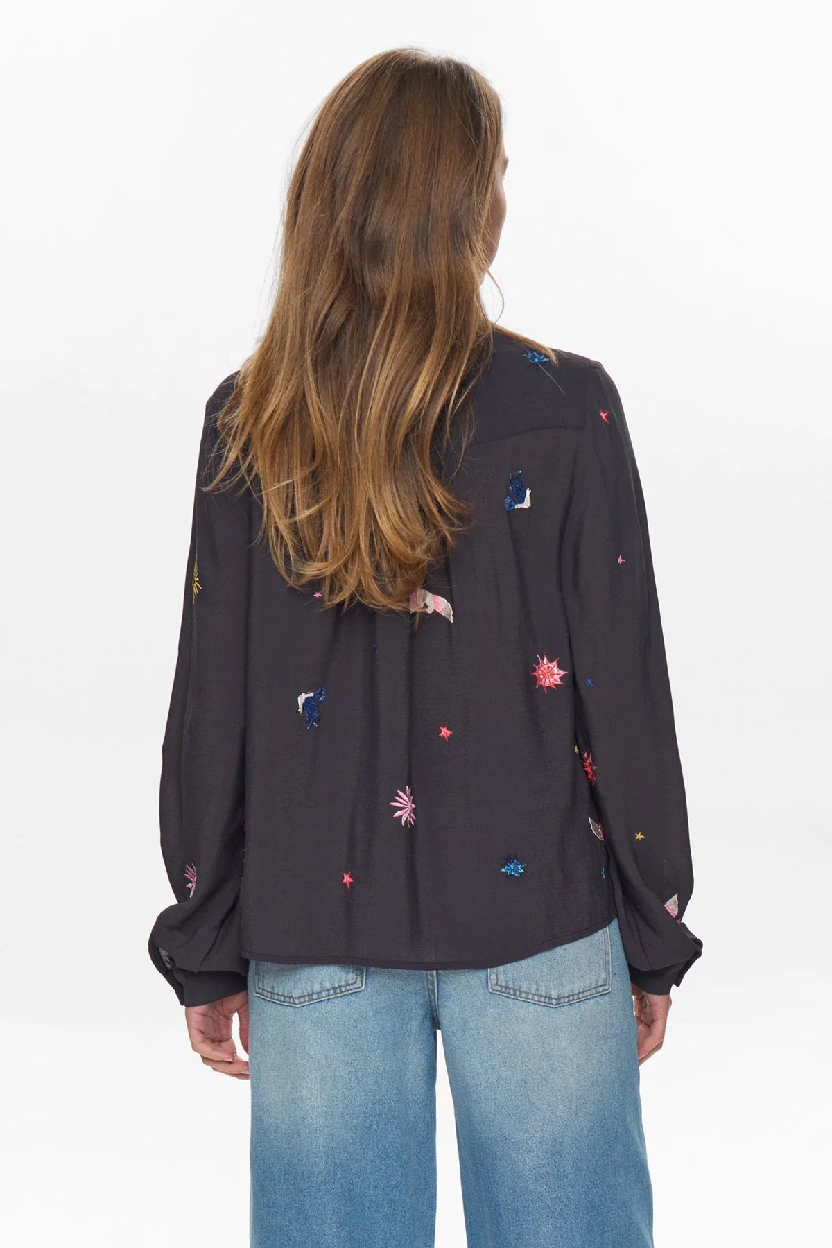 Person wearing a black blouse with colorful embroidery and blue jeans on a white background