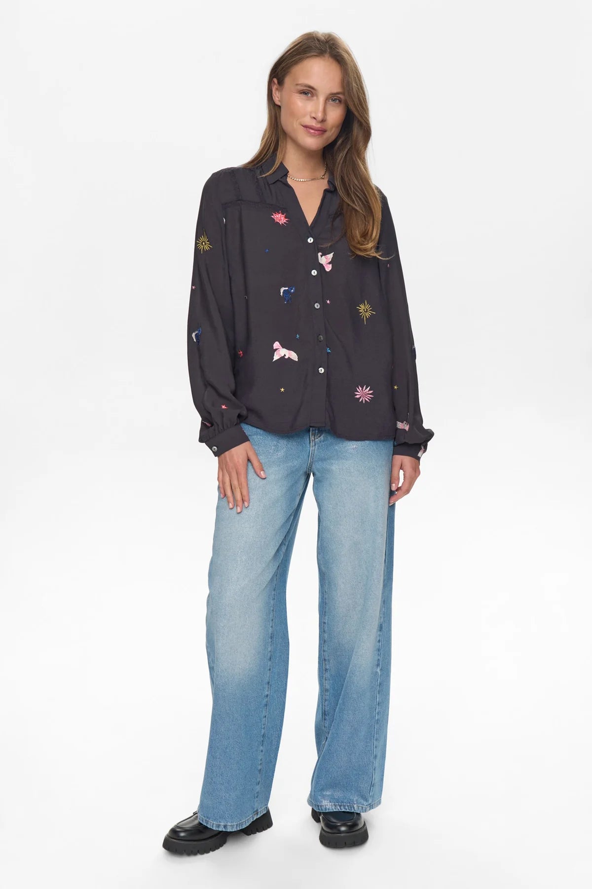 Woman wearing a black embroidered shirt and blue jeans on a white background