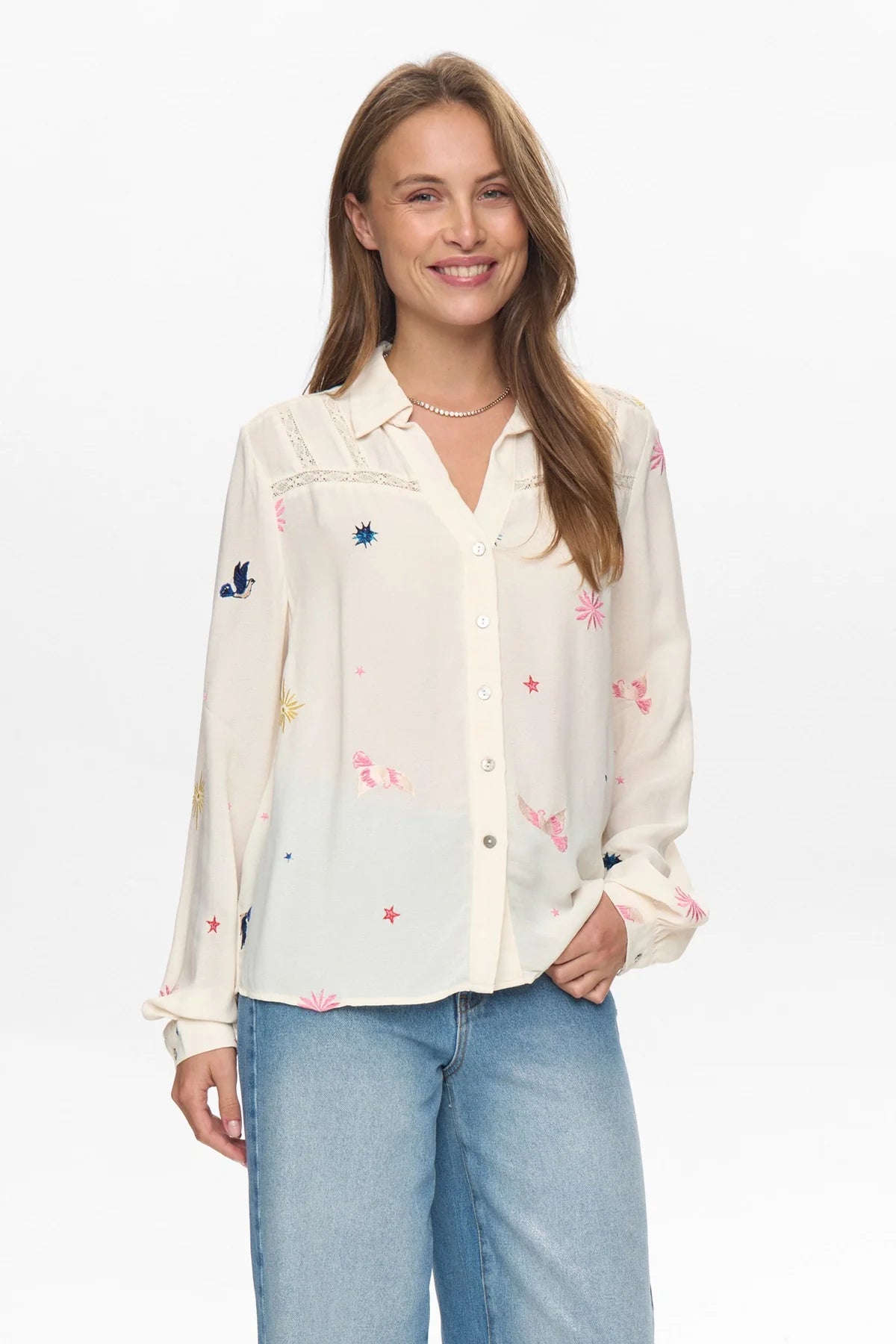 Woman wearing a white blouse with colorful embroidery and blue jeans on a white background