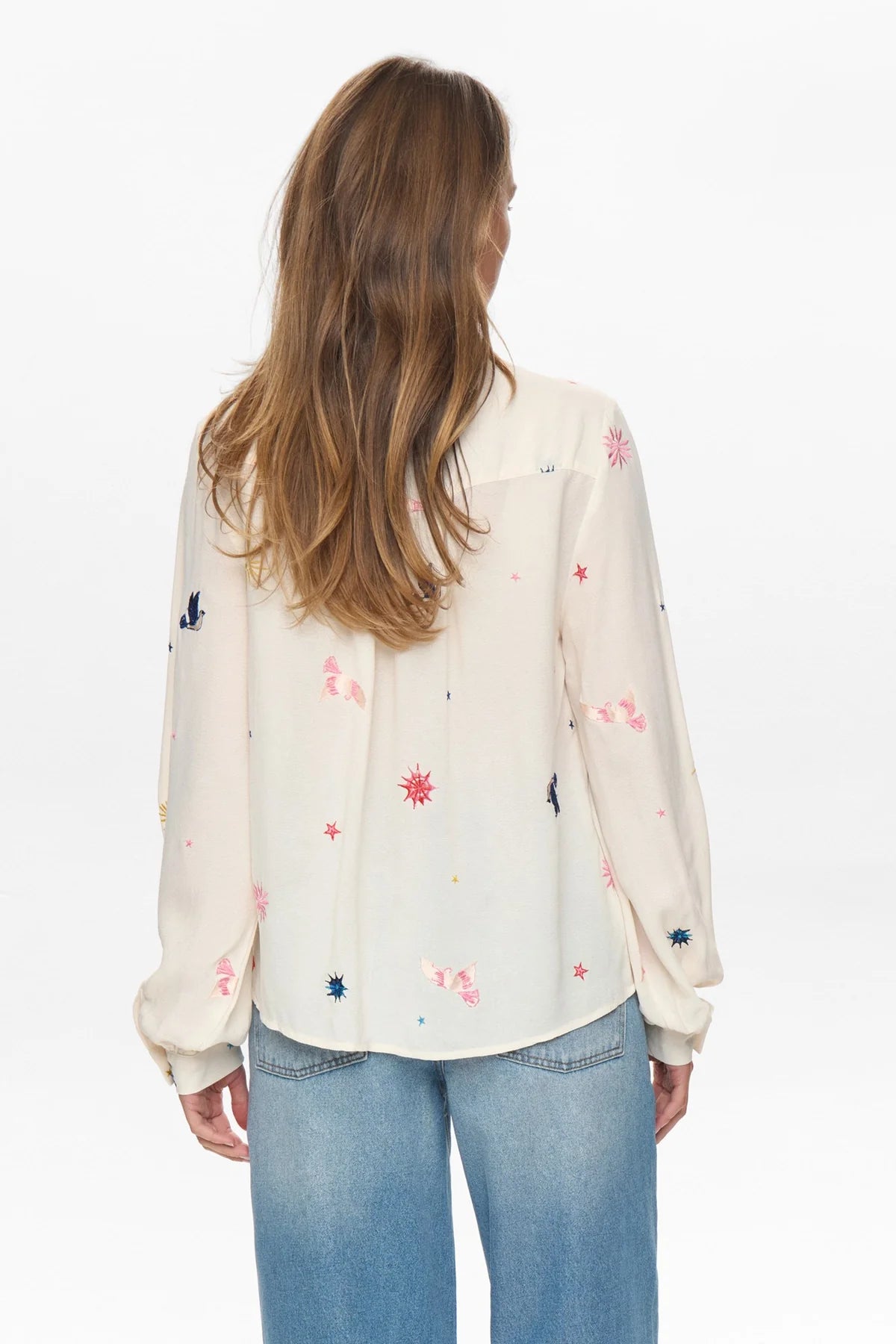 Woman wearing a cream blouse with colorful floral patterns and blue jeans on a white background