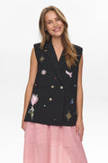 Woman wearing a black embroidered vest over a pink dress on a white background