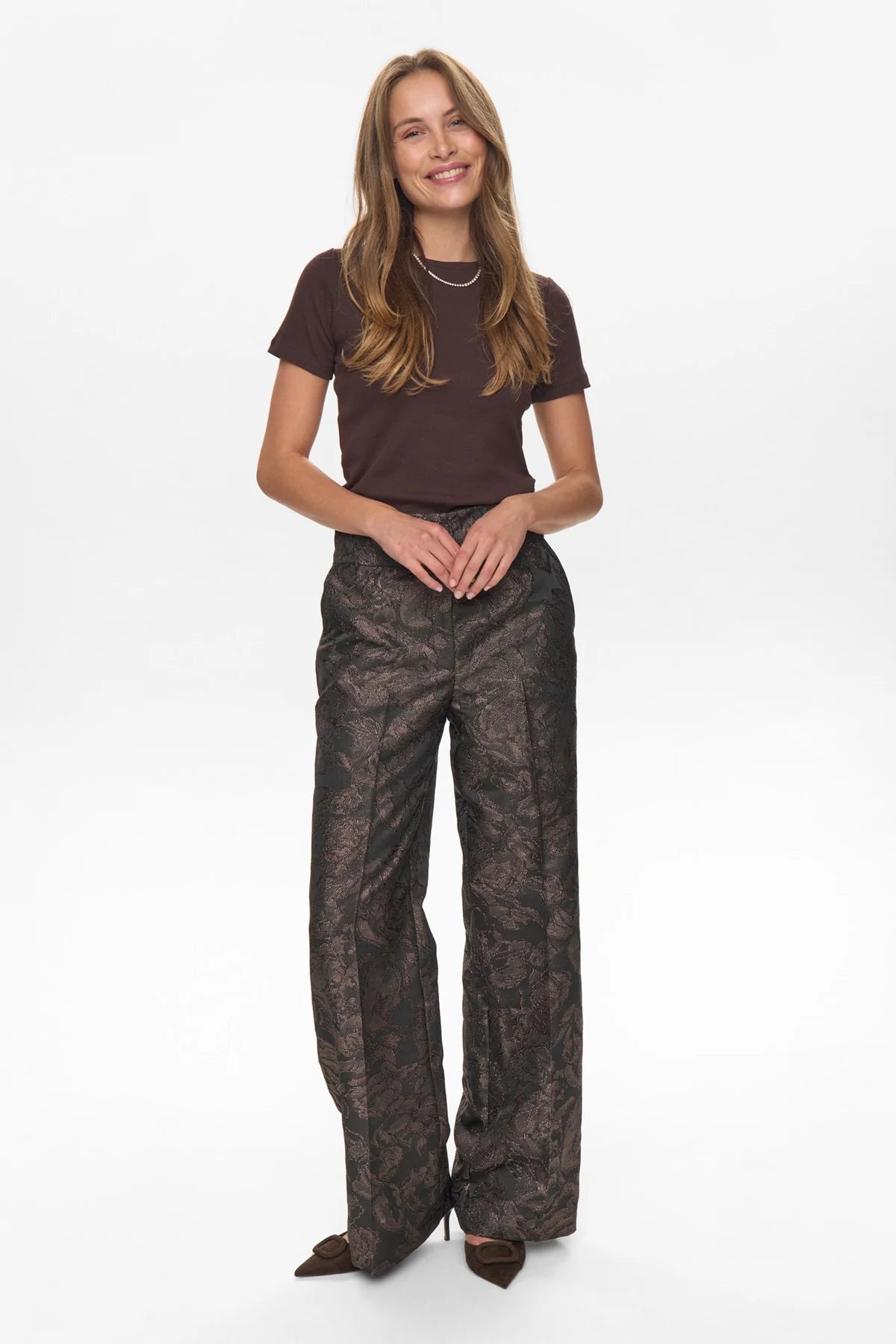 Woman wearing a brown t-shirt and patterned pants on a white background