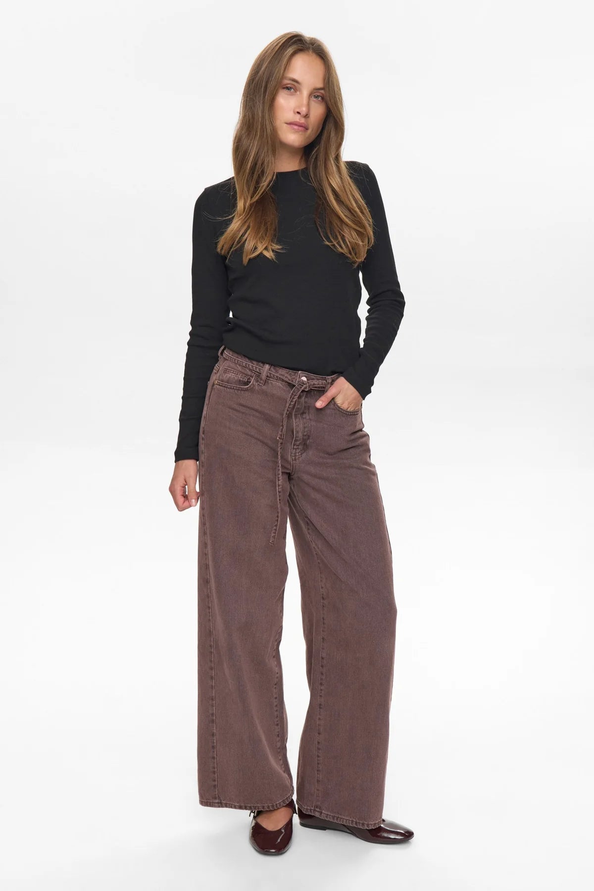 Woman wearing a black top and brown wide-leg pants on a white background