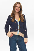 Woman wearing a navy cardigan with beige accents and blue jeans on a white background