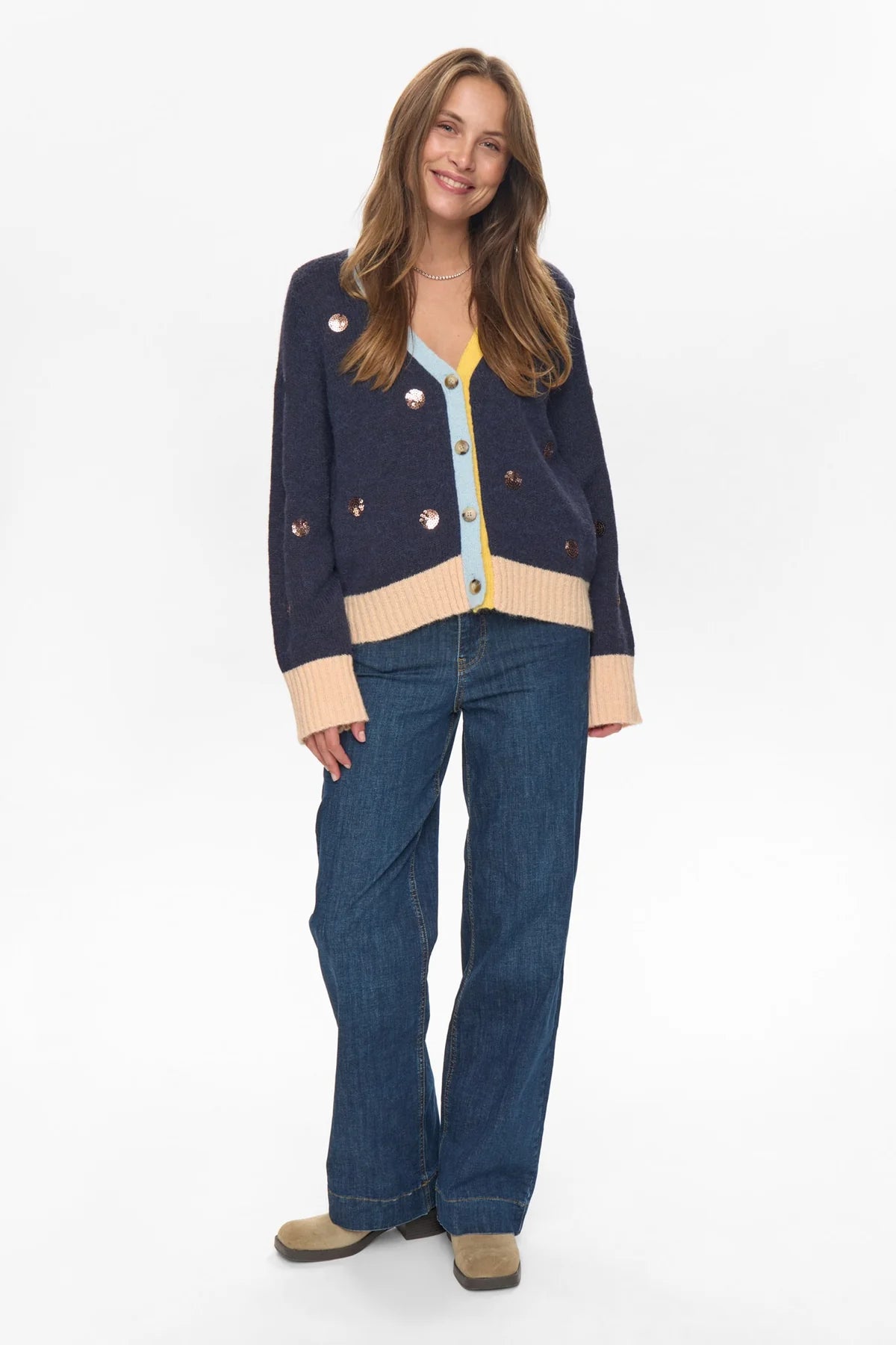 Woman wearing a navy cardigan with beige accents and blue jeans on a white background
