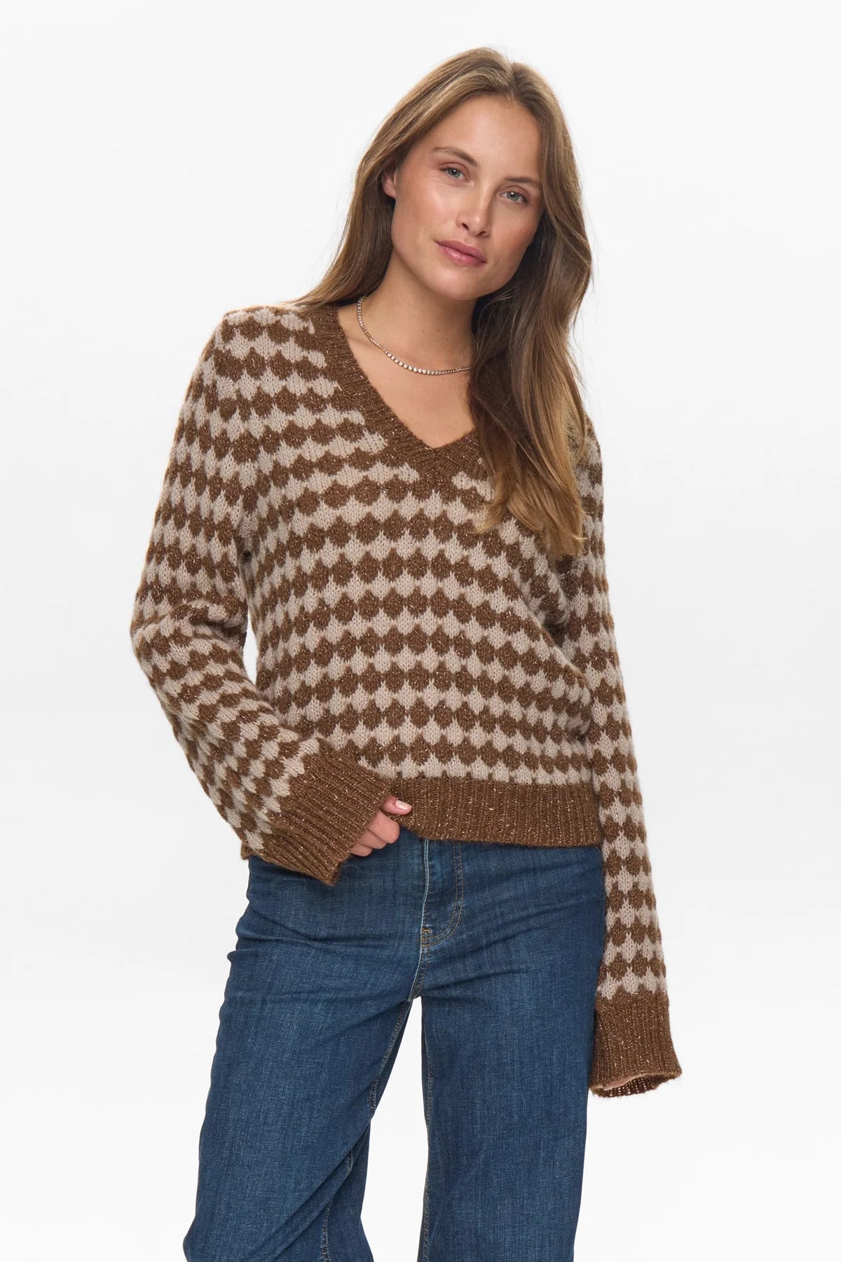Woman wearing a brown and beige patterned sweater with blue jeans on a white background