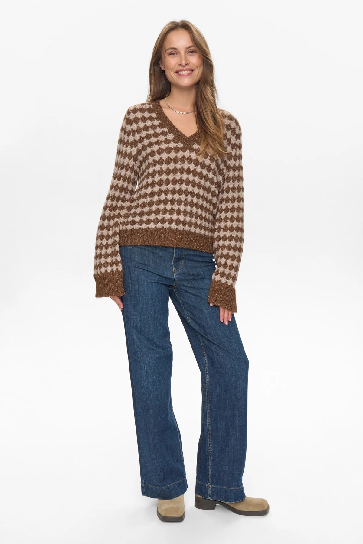 Woman wearing a brown and beige checkered sweater and blue jeans on a white background