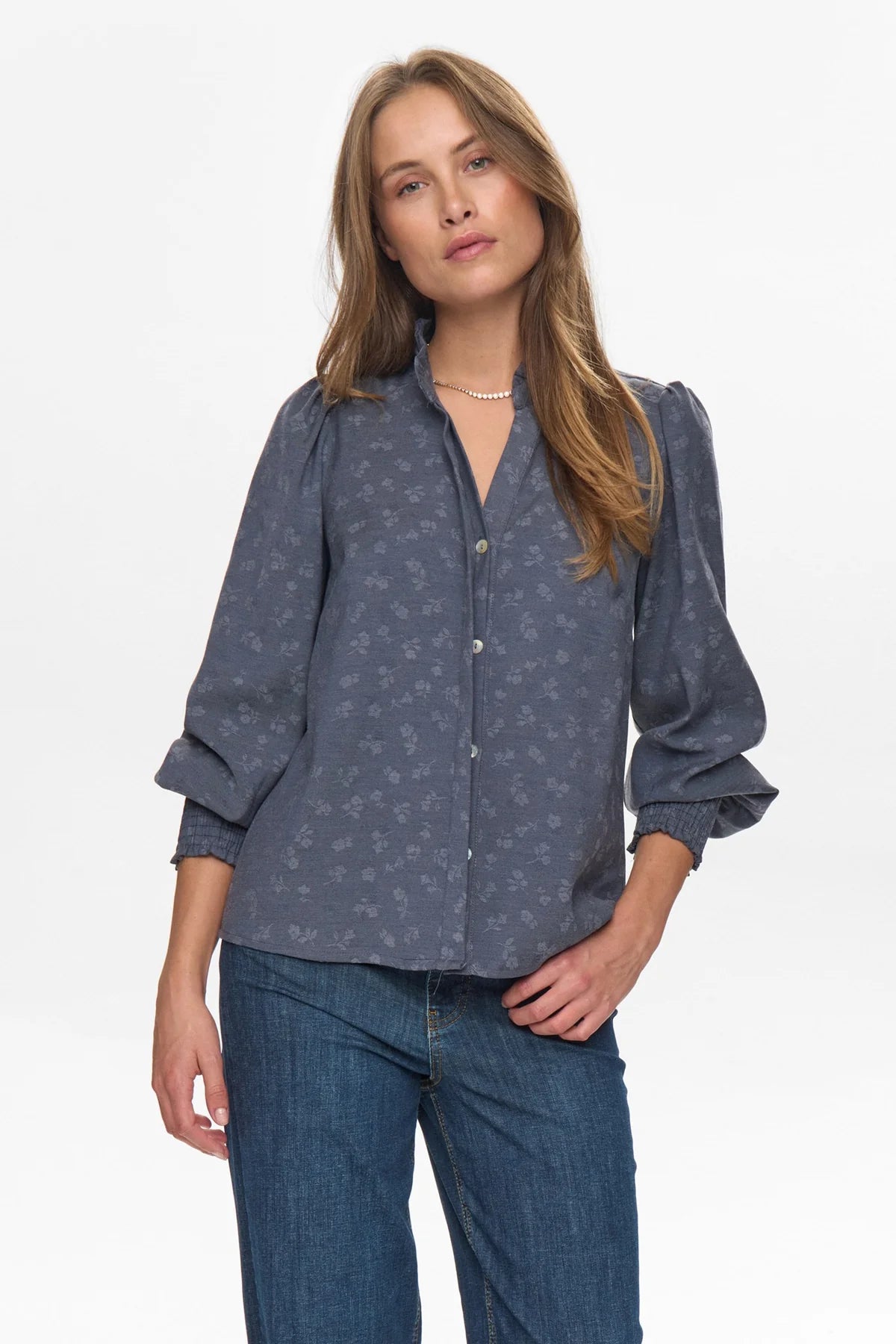 Woman wearing a blue patterned blouse and jeans on a white background