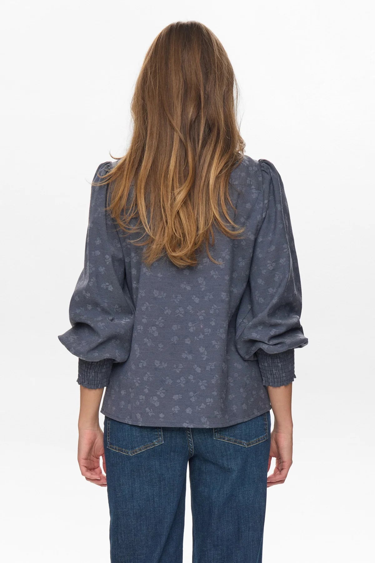 Person wearing a blue patterned blouse and jeans on a white background
