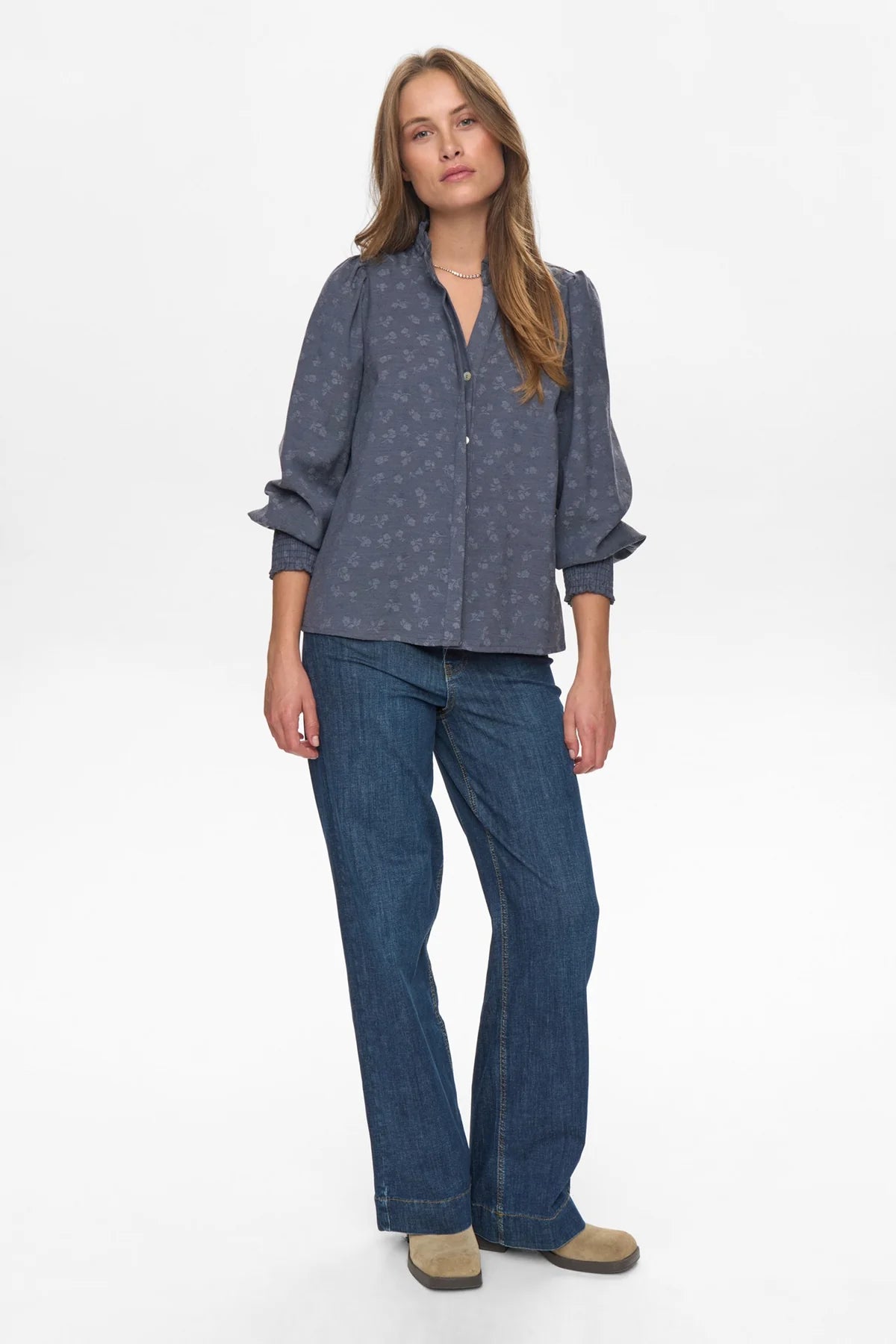 Woman wearing a blue patterned shirt and jeans on a white background