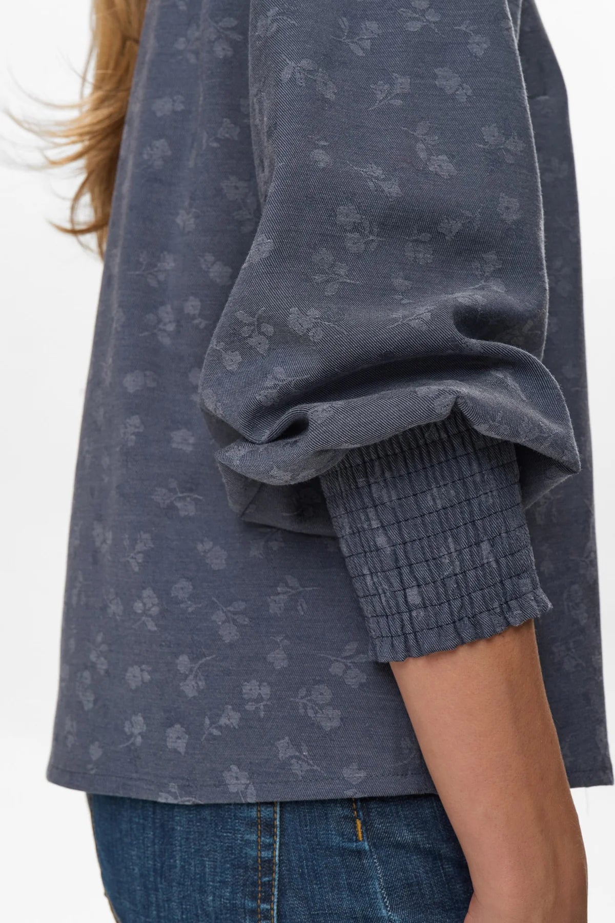 Person wearing a dark blue patterned shirt with rolled-up sleeves on a white background