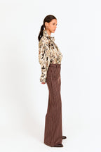 Woman wearing a patterned blouse and brown striped pants on a white background