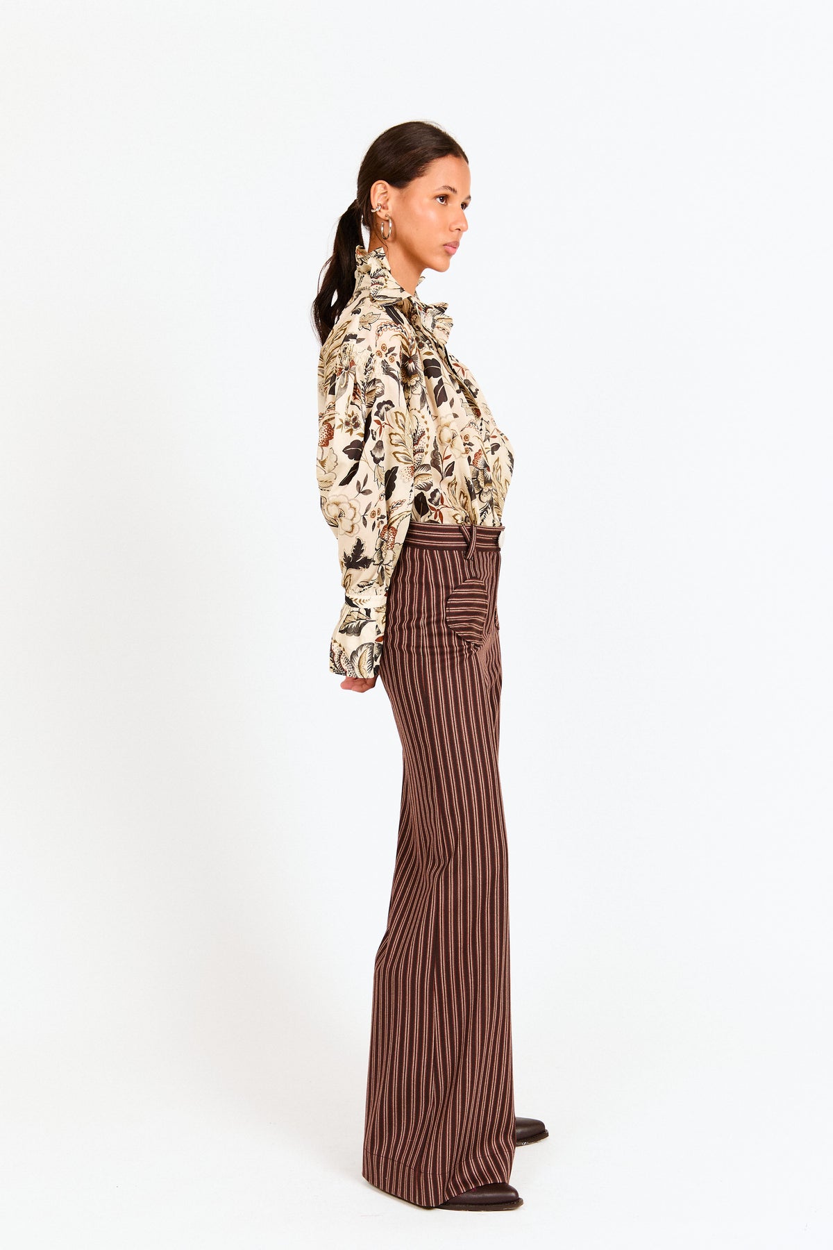 Woman wearing a patterned blouse and brown striped pants on a white background
