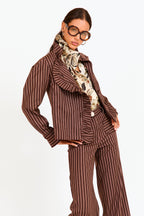 Woman wearing a brown pinstripe outfit with a patterned scarf on a white background