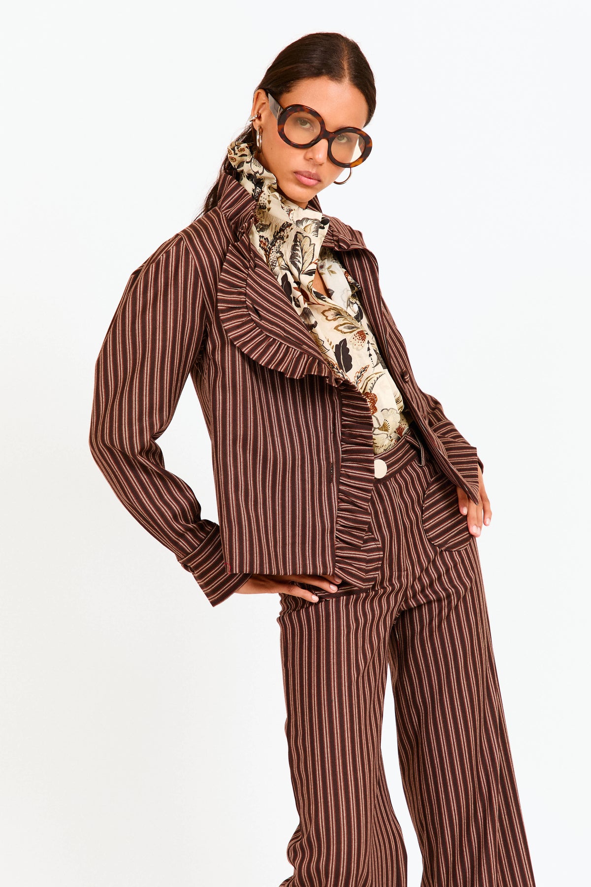 Woman wearing a brown pinstripe outfit with a patterned scarf on a white background