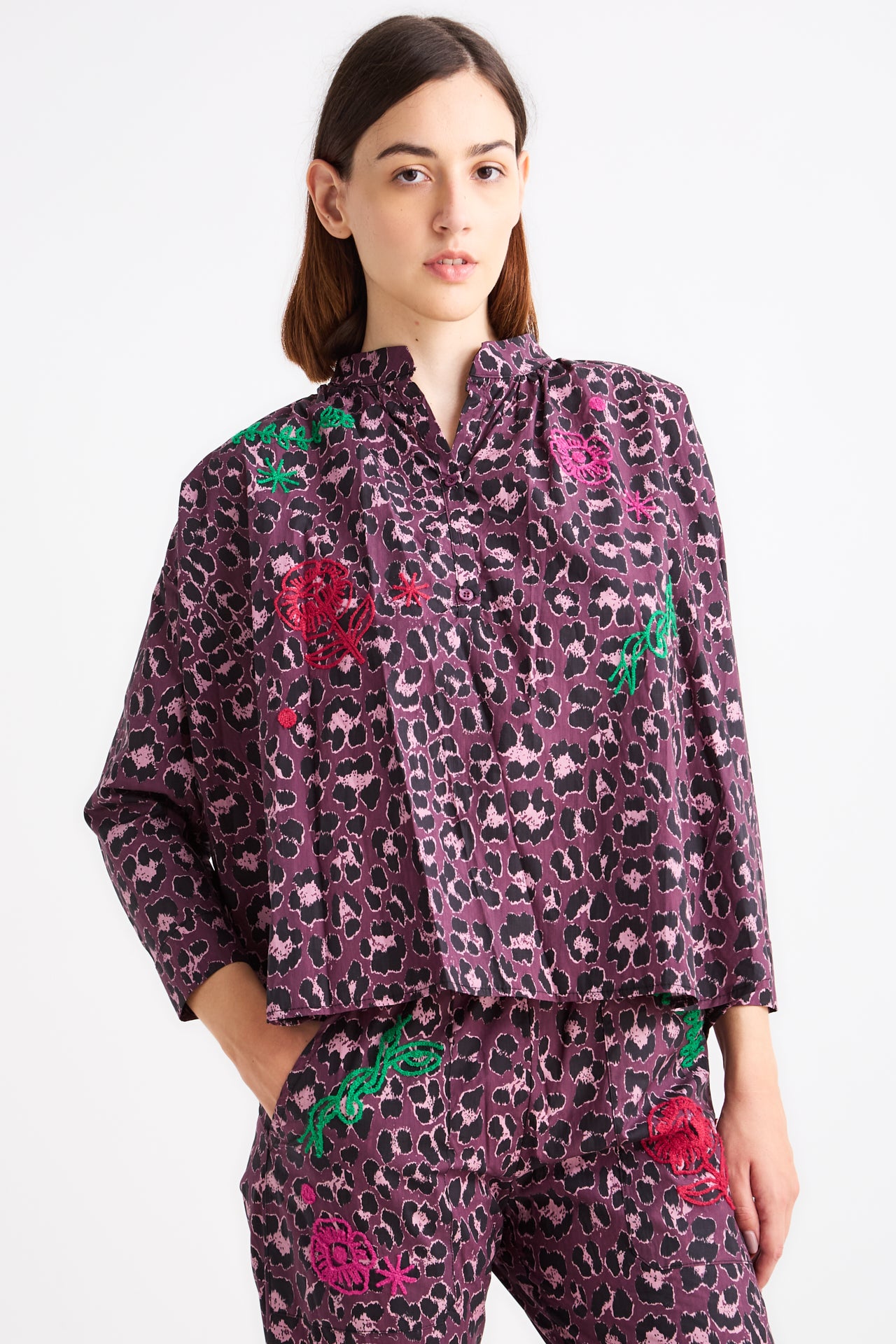 Woman wearing a purple patterned outfit with floral embellishments on a white background