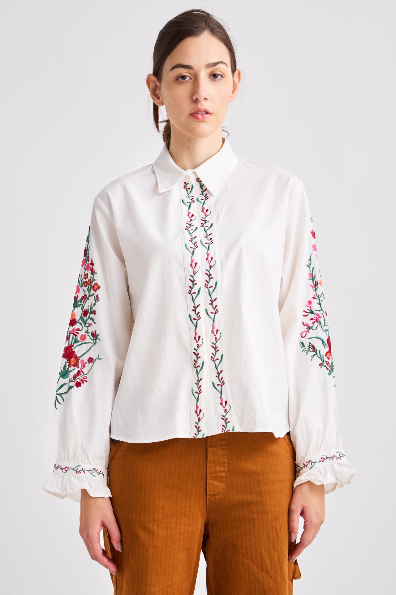Woman wearing a white blouse with floral embroidery on a plain background