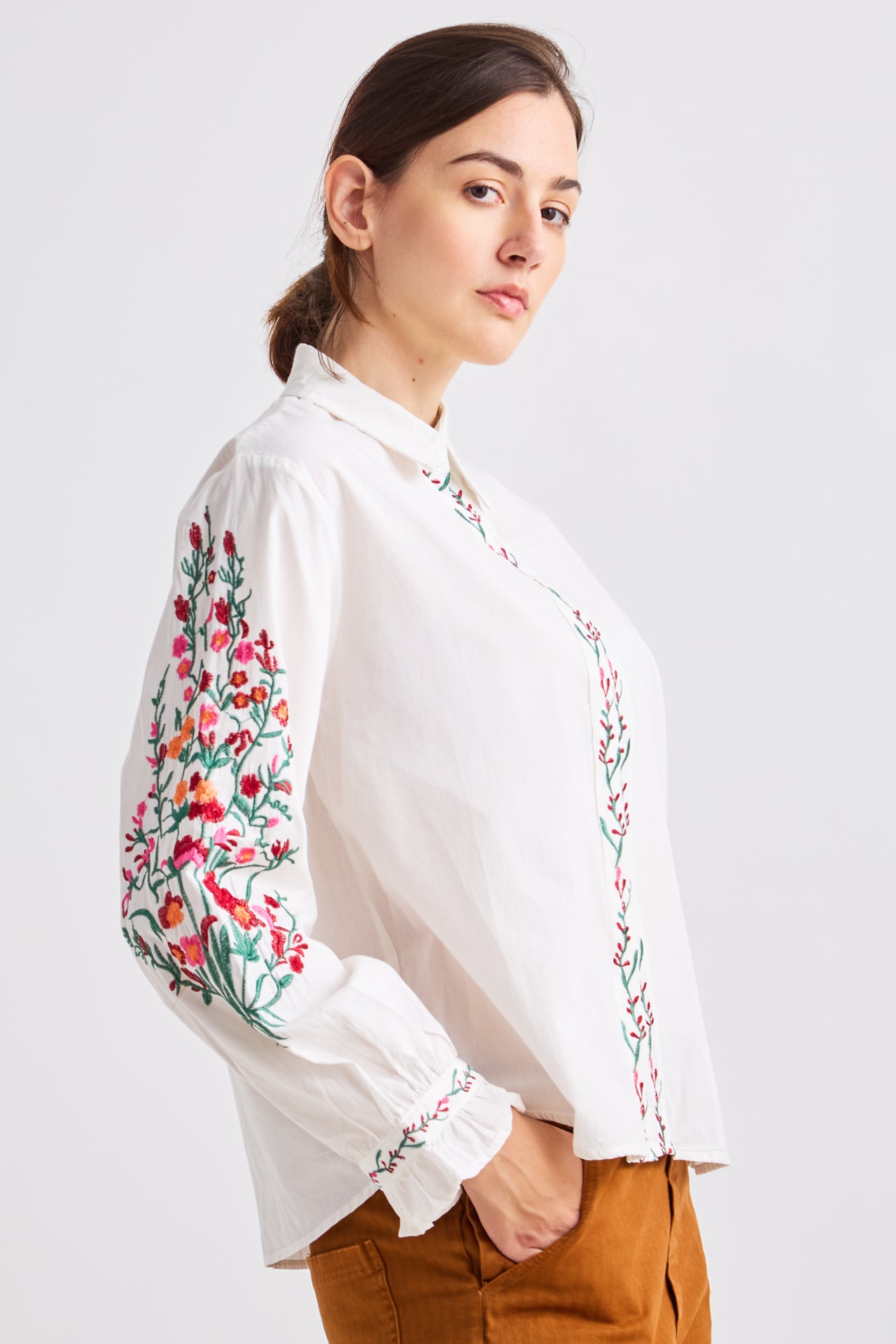 Woman wearing a white blouse with colorful floral embroidery on a plain background