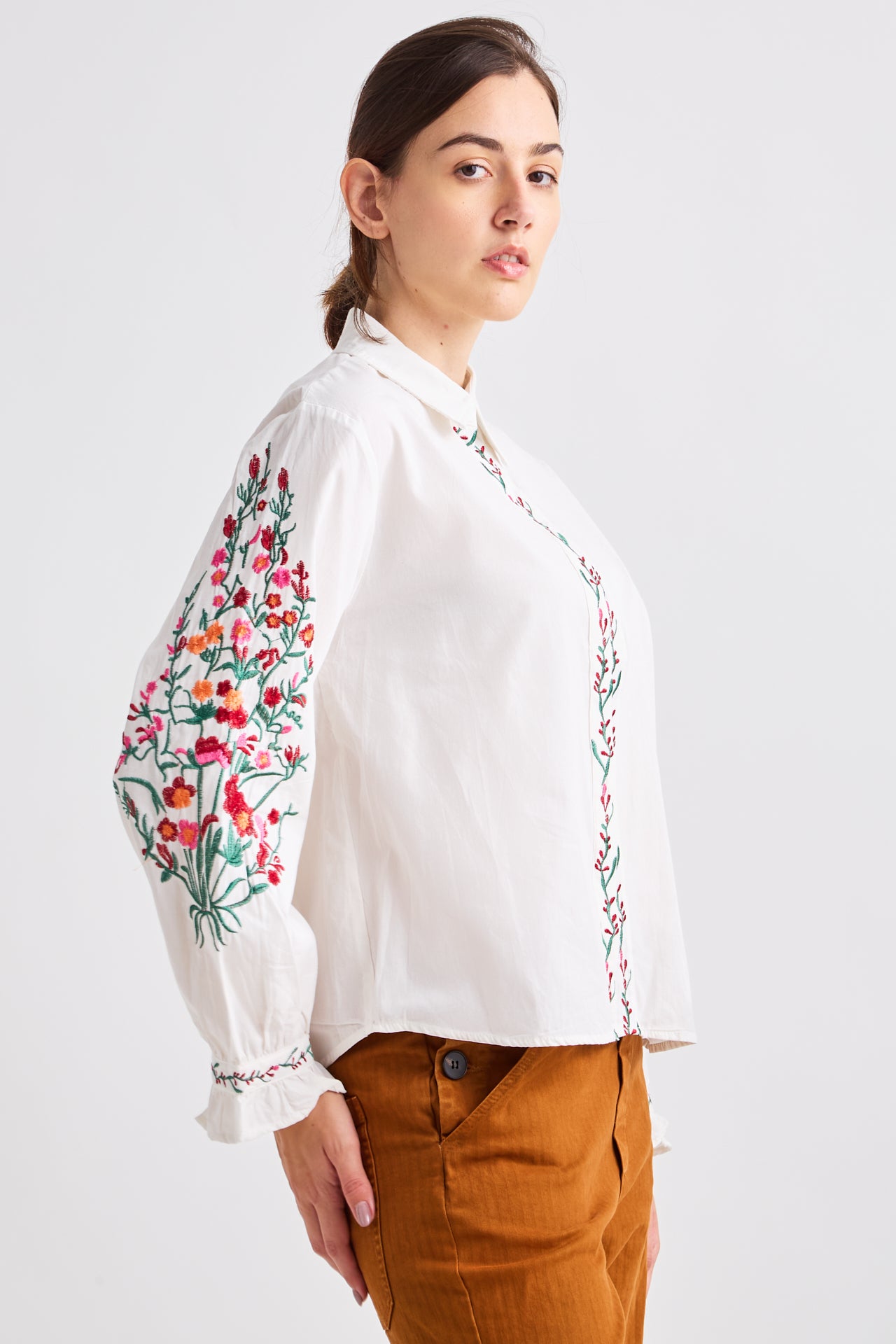 Woman wearing a white blouse with floral embroidery on a plain background