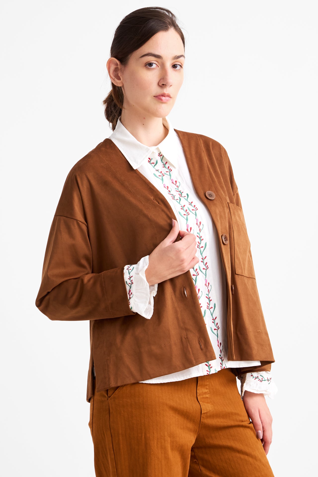 Woman wearing a brown blazer over a white shirt with floral embroidery on a white background