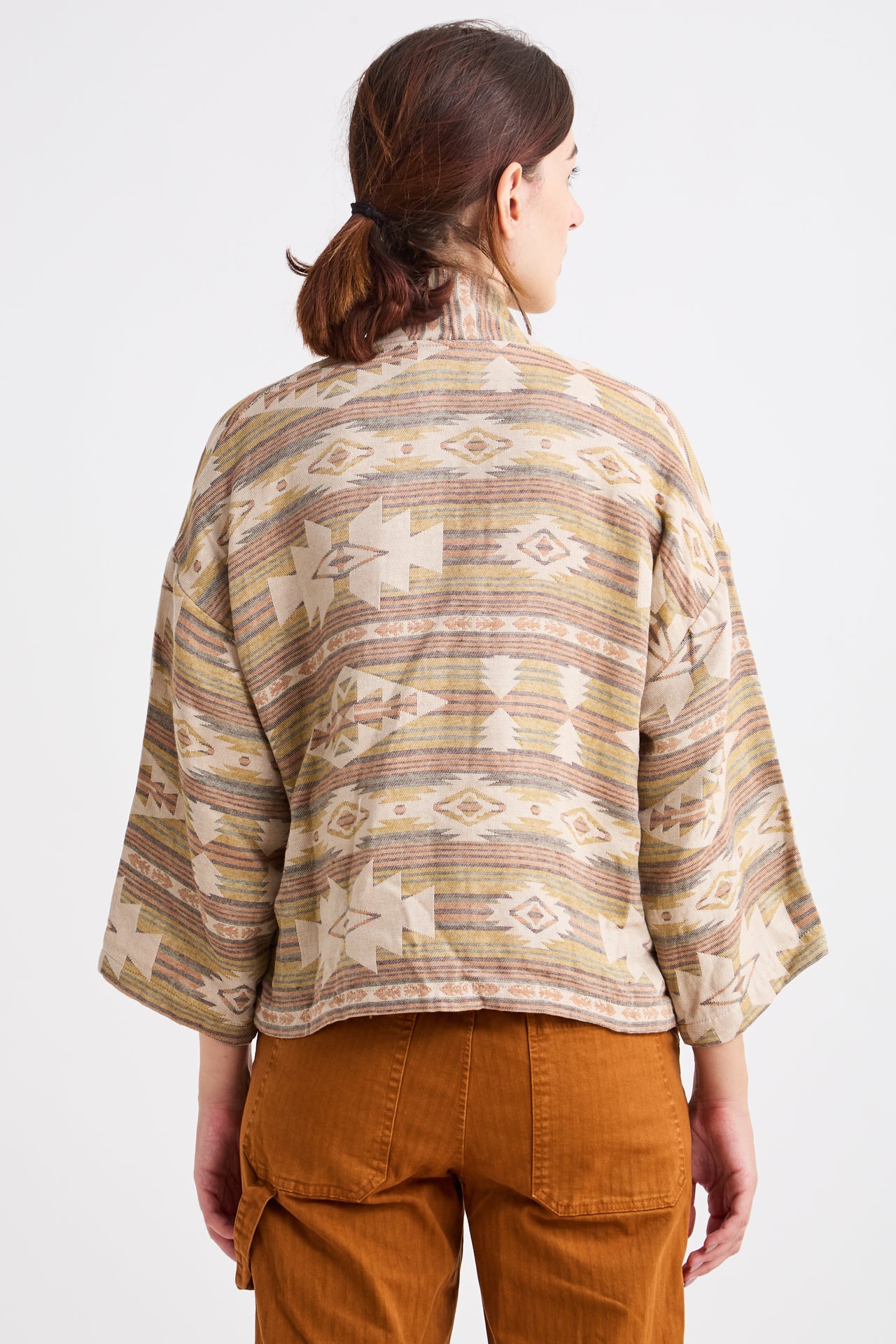 Person wearing a patterned shirt and brown pants on a white background