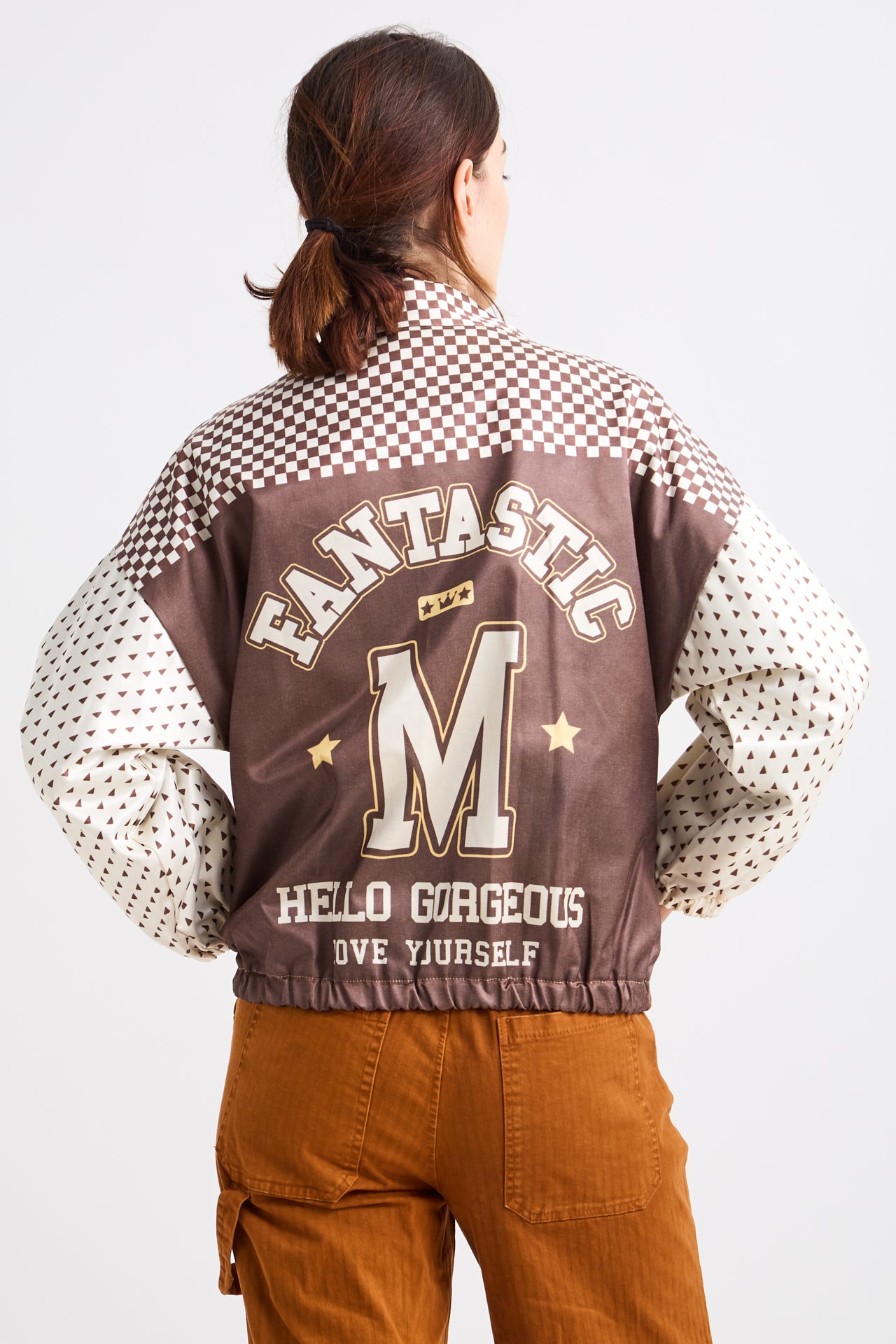 Person wearing a brown varsity jacket with checkered sleeves and text on a white background