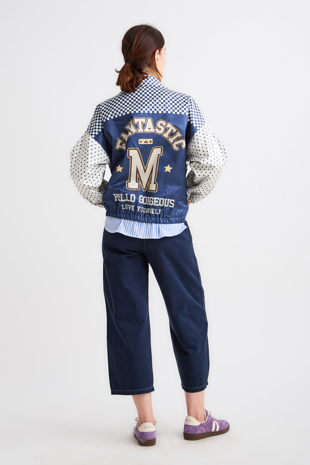 Person wearing a blue varsity jacket with lettering on a white background