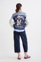 Person wearing a blue varsity jacket with lettering on a white background