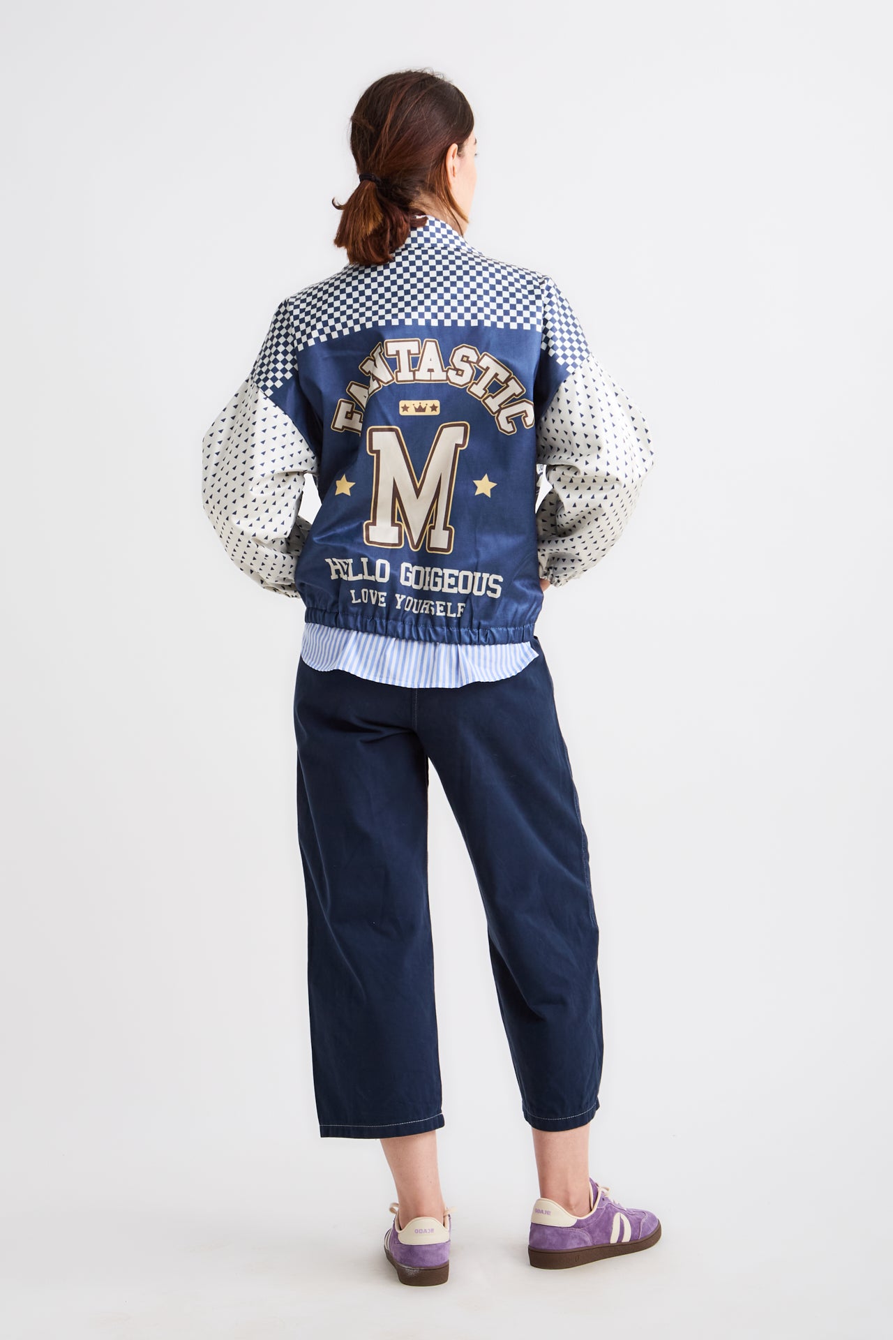 Person wearing a blue varsity jacket with lettering on a white background