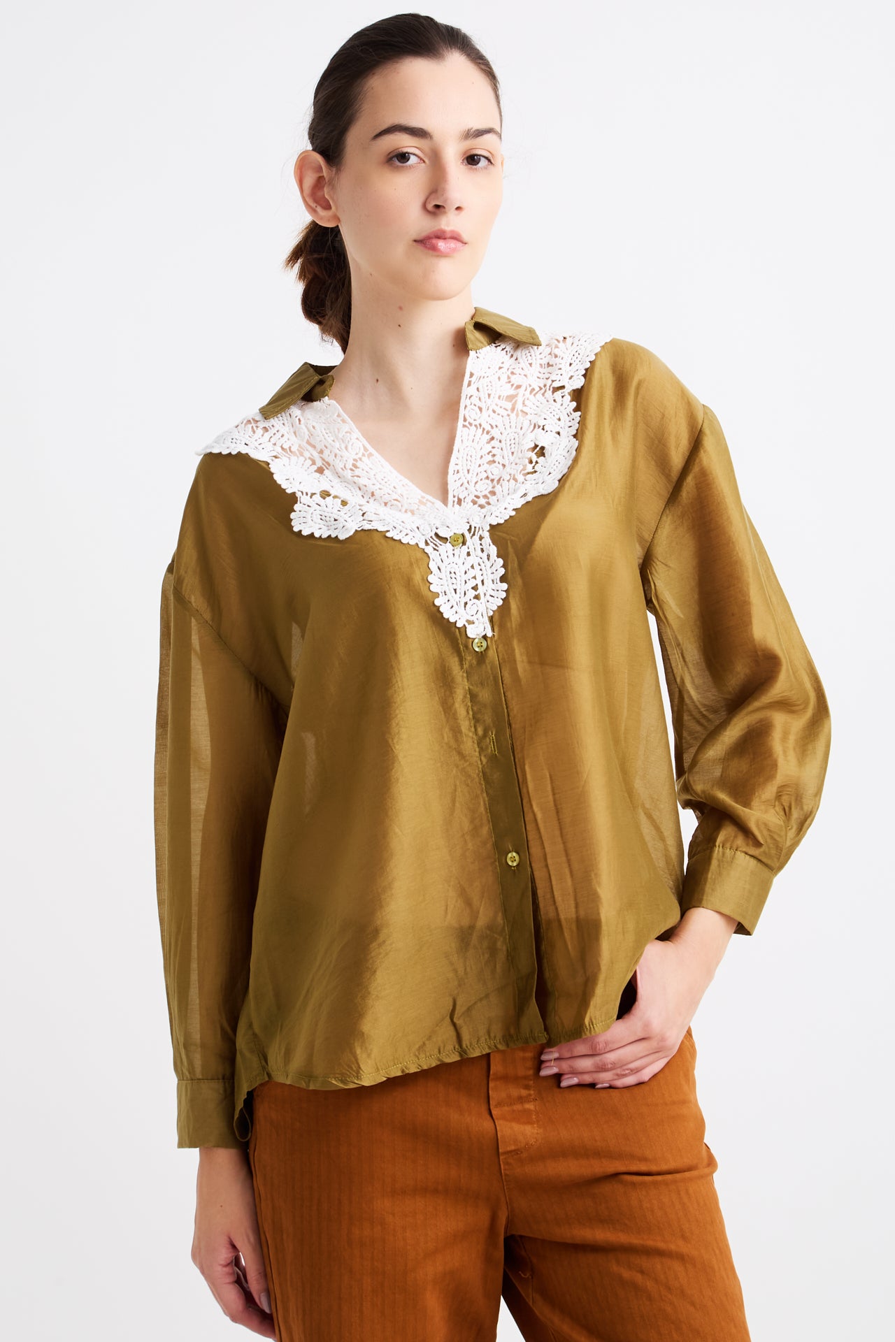 Woman wearing a mustard yellow blouse with lace collar and brown pants on a white background