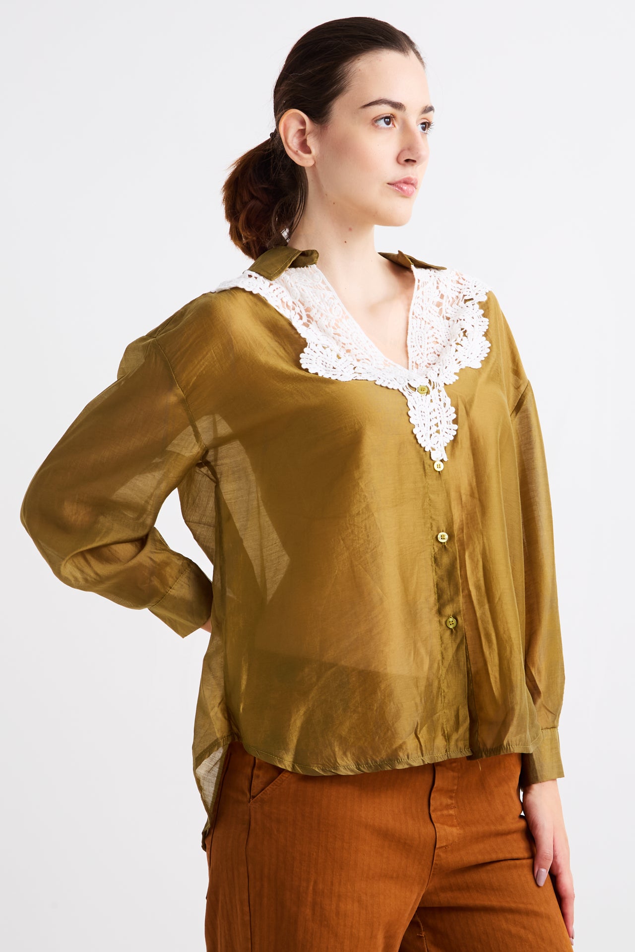 Woman wearing a mustard yellow blouse with lace details on a white background