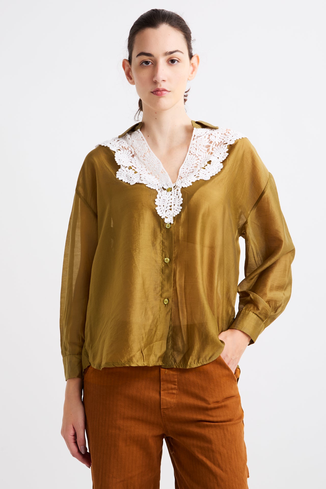 Woman wearing a mustard yellow blouse with lace details on a white background