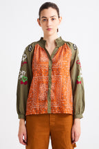 Person wearing a green and orange patterned shirt with embroidered details on a white background
