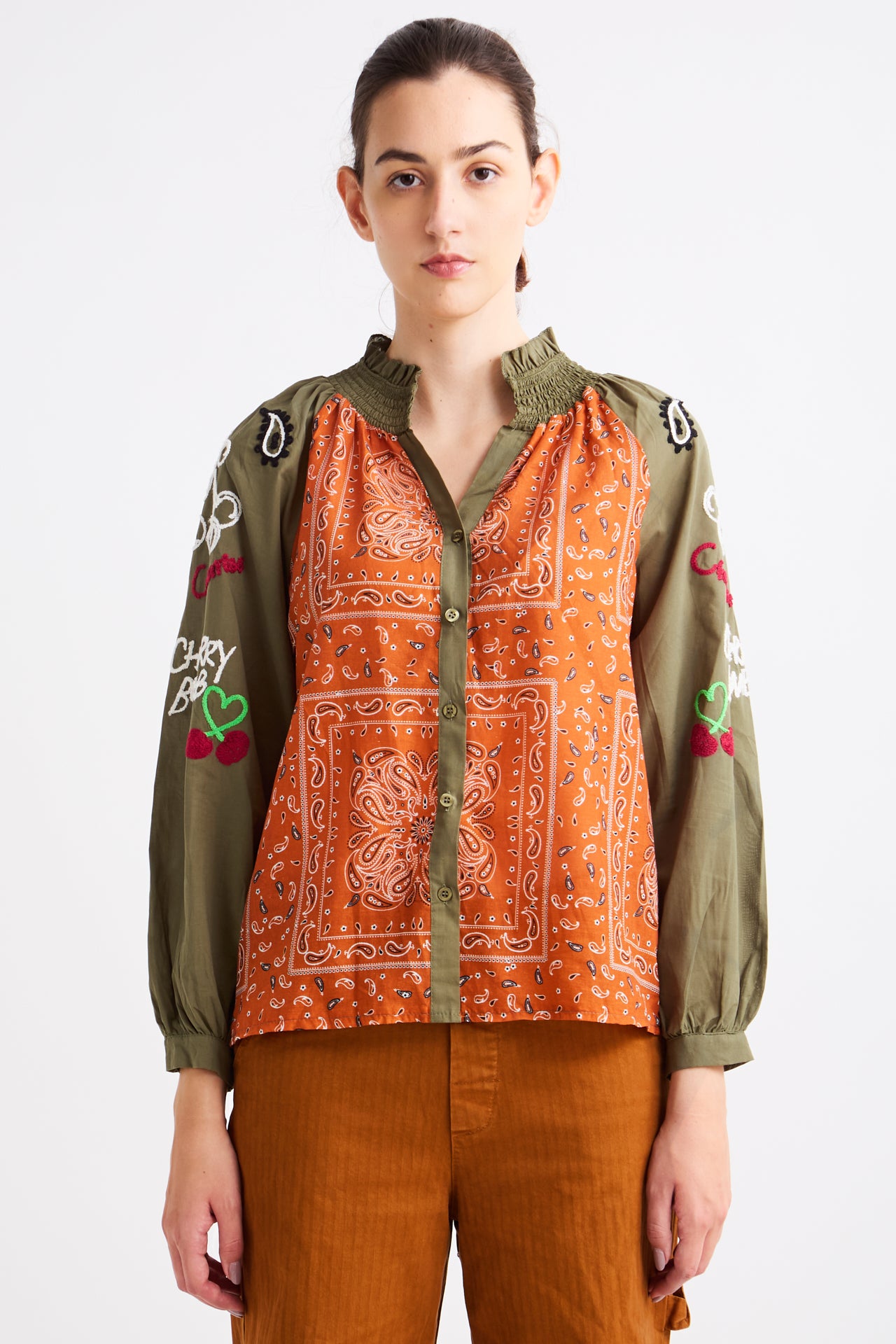 Person wearing a green and orange patterned shirt with embroidered details on a white background