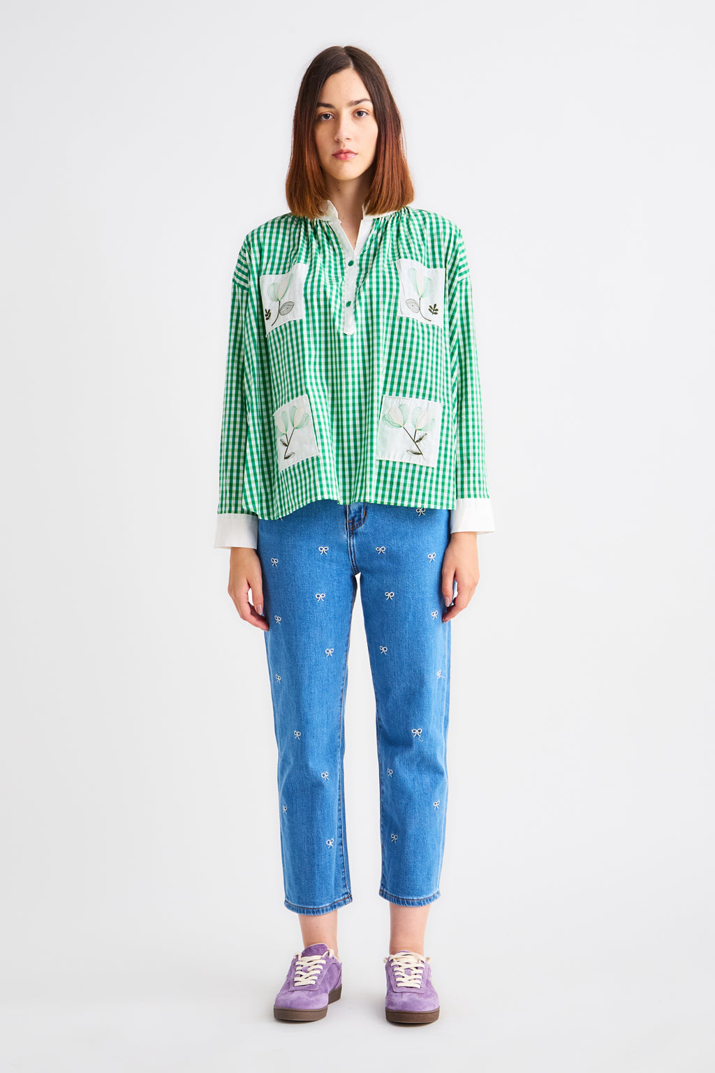 Person wearing a green checkered shirt with white patches and blue jeans on a white background