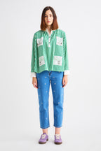 Person wearing a green checkered shirt with white patches and blue jeans on a white background