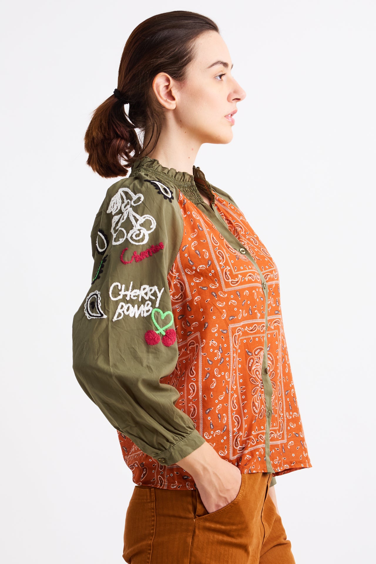 Woman wearing a green embroidered sweater over an orange patterned shirt on a white background