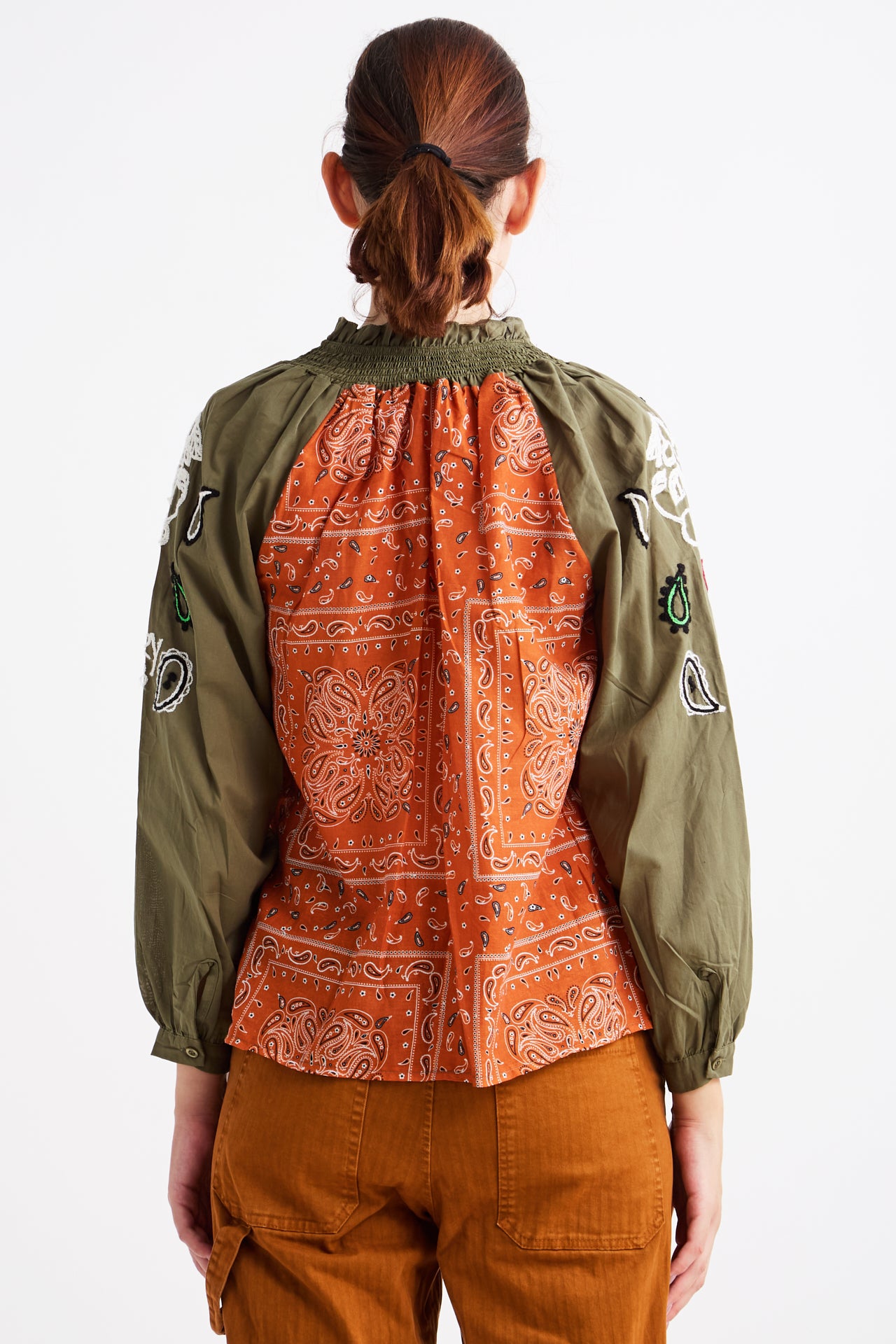 Person wearing a green jacket with orange bandana pattern on the back, standing against a white background