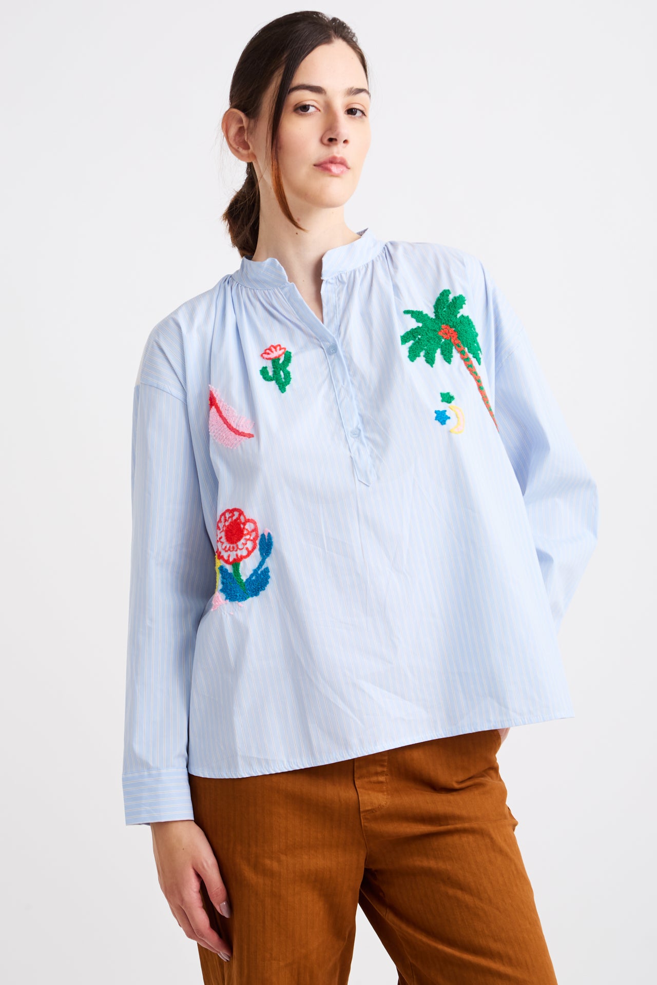 Woman wearing a light blue shirt with colorful embroidered designs on a white background