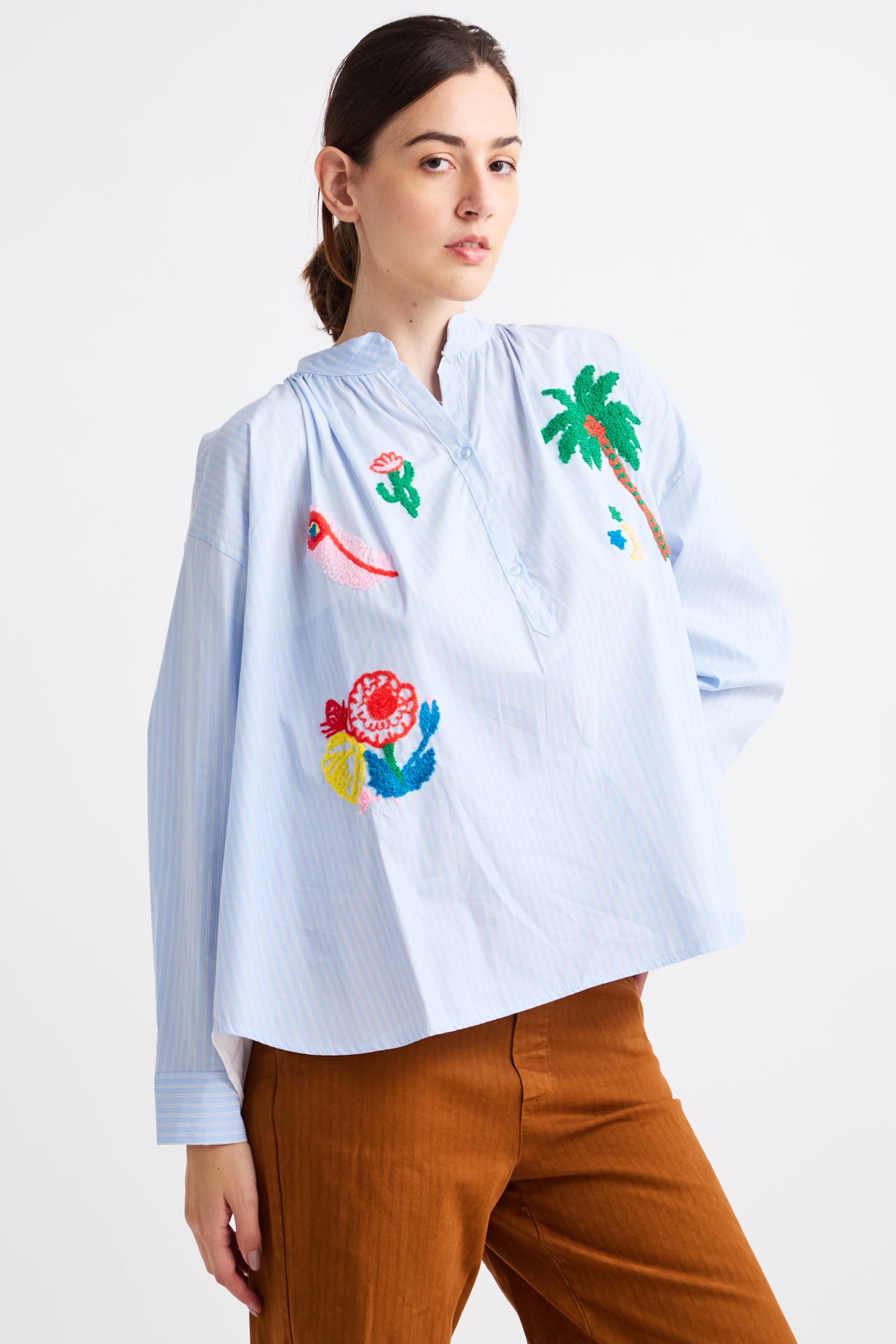 Woman wearing a light blue shirt with colorful floral and bird designs on a white background