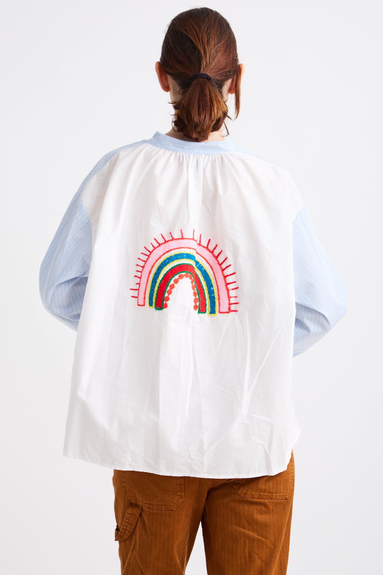 Person wearing a white cape with a rainbow design on the back, standing against a plain background.