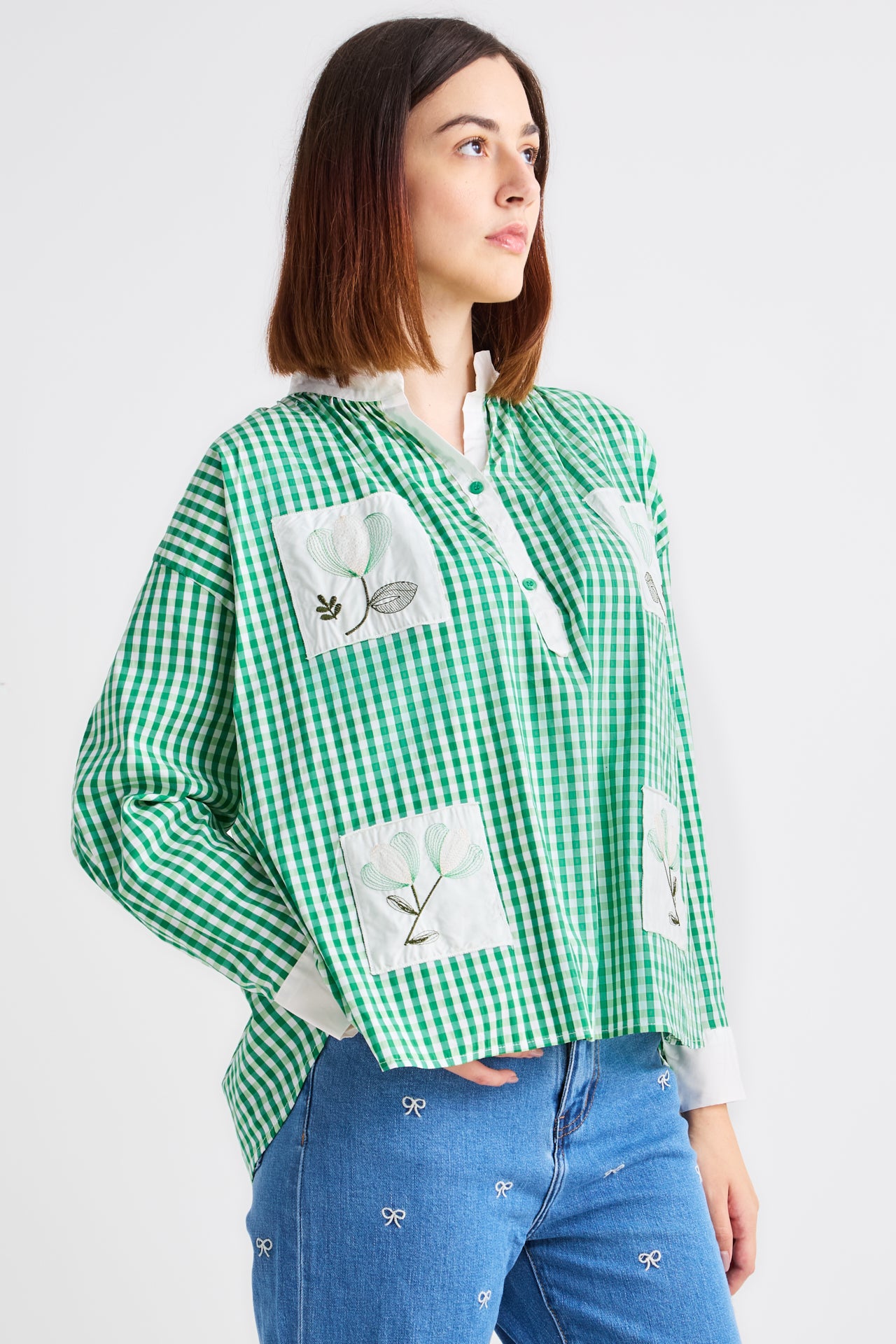 Woman wearing a green checkered shirt with floral patches on a white background