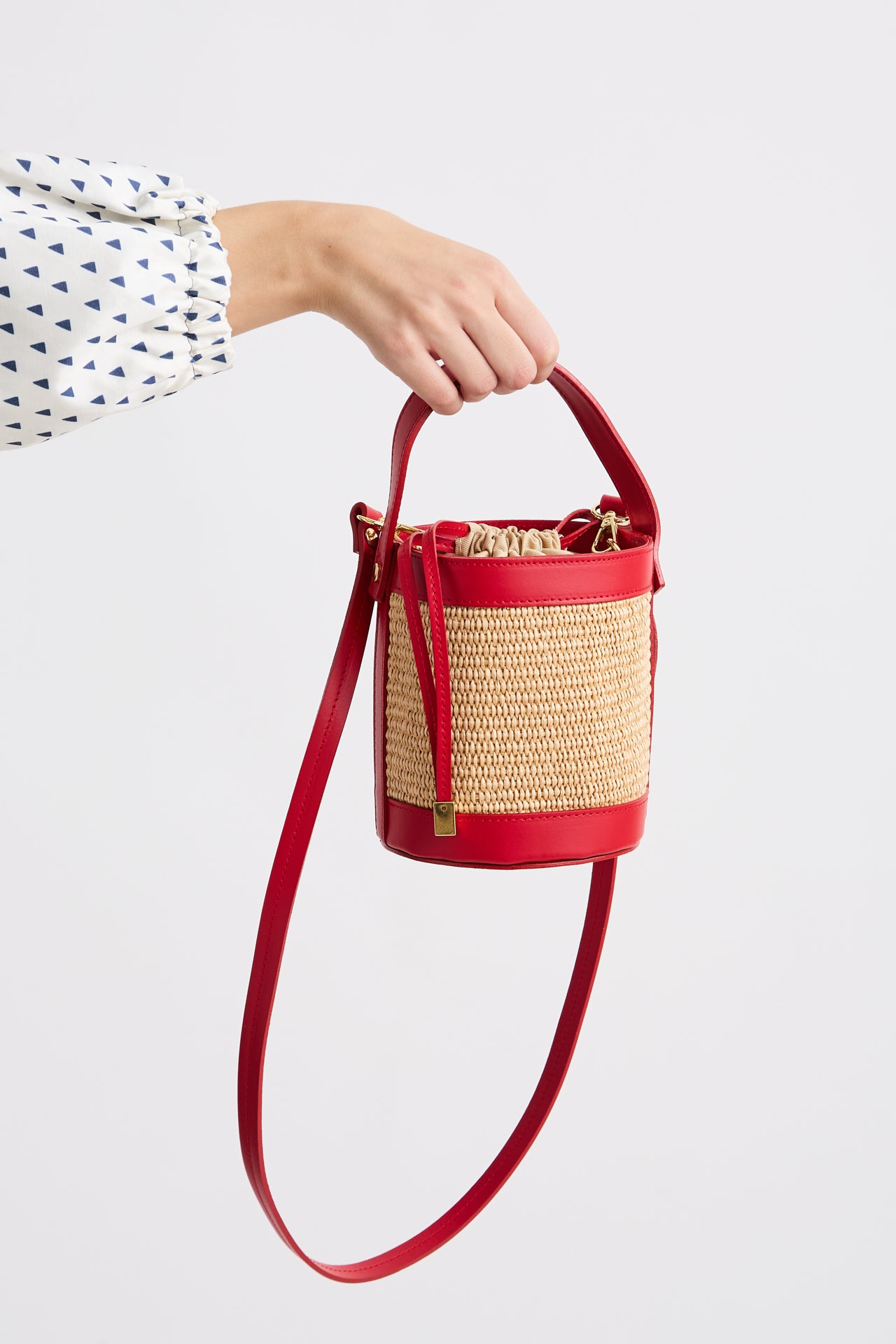 Red and straw handbag held by a person on a light gray background